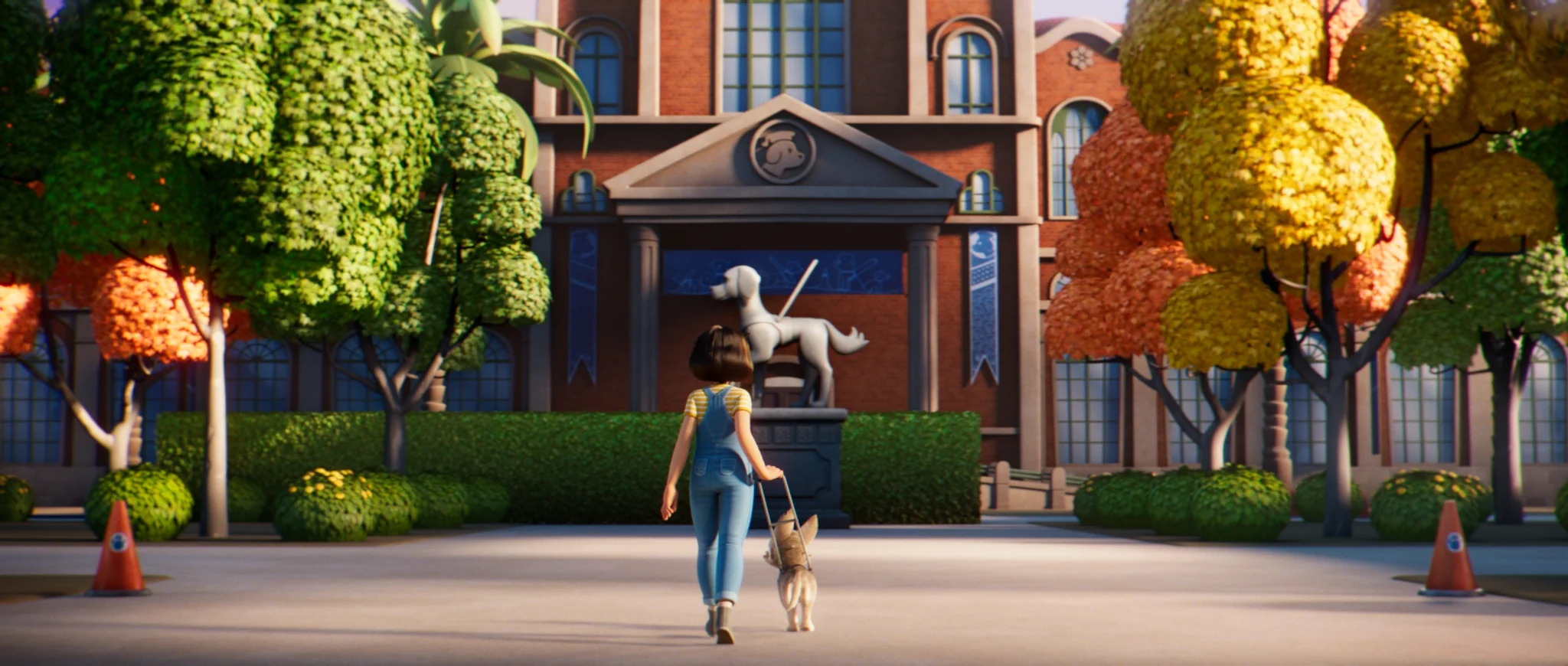 A girl in denim overalls walks a small dog in a harness towards a red-brick building with a guide dog statue at its entrance.